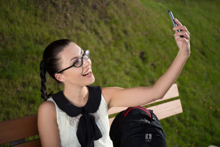 happy beautiful school girl making selfie photo on smartphone in summer parkの写真素材