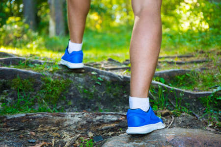 hiking concept - close up of male legs in running shoes in forest