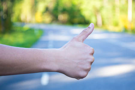 close up of male hand hitchhiking on forest roadの写真素材