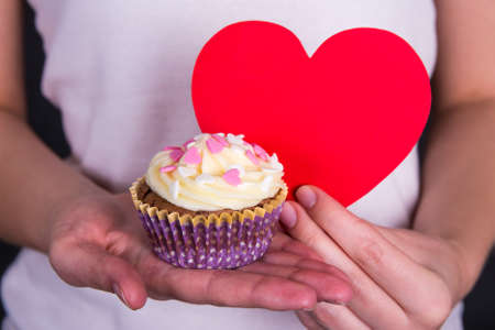 valentine's day concept - sweet colorful cupcake and red heart in female handsの写真素材