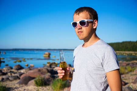 young handsome man with bottle of beer on the beachの写真素材