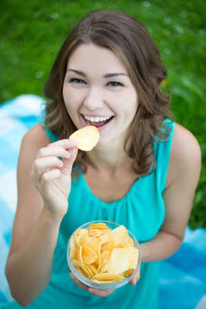cute woman eating potato chips in summer parkの写真素材