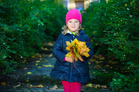 happy little girl in warm clothes with yellow leaves posing in autumn parkの写真素材