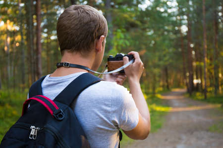 back view of man taking a photo with retro camera in forest