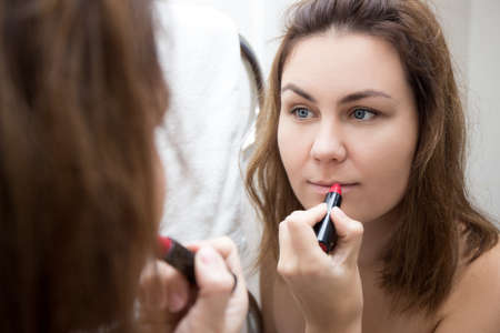close up of woman looking at mirror and applying lipstick on her lipsの写真素材