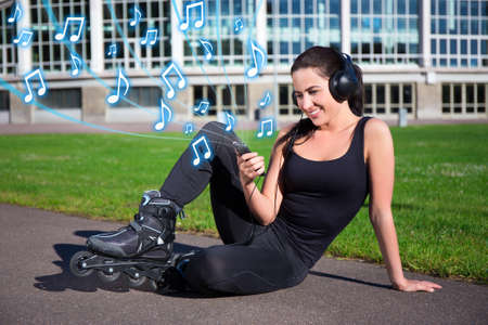 pretty woman in roller skates sitting and listening music in summer park