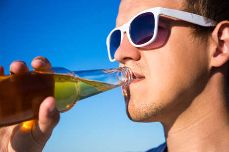 close up portrait of handsome man drinking beer over sky backgroundの写真素材