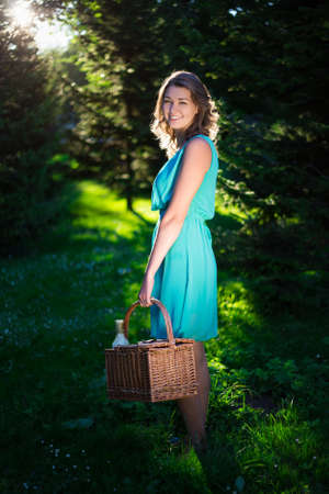 young beautiful woman with picnic basket and bottle of wine in evening summer forestの写真素材