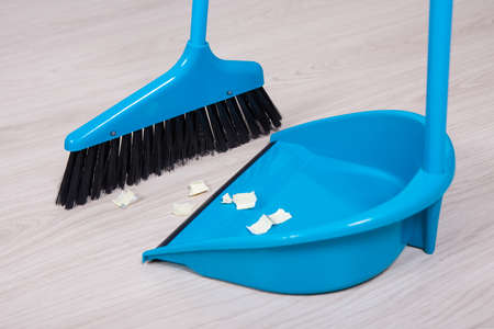 close up of broom and dustpan with paper trash on wooden floorの写真素材