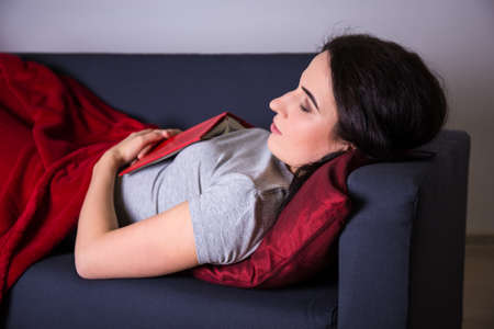 young beautiful woman sleeping with book on sofa at home