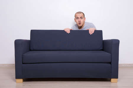 young man hiding behind a sofa at home