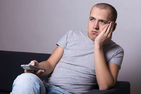 young bored man sitting on sofa and watching movie or tv