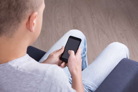 back view of young man using smart phone at homeの写真素材