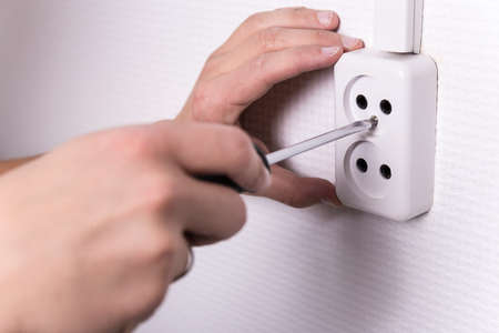 close up of male hands with screwdriver installing electrical socket on wall
