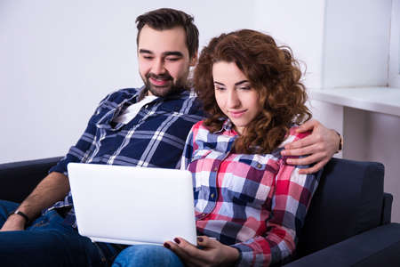 happy young couple with laptop on sofa at homeの写真素材