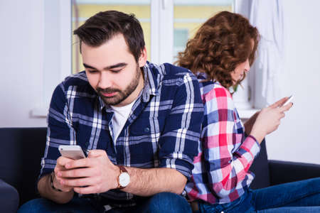 relationship and phone addiction concept - young couple using their smart phones at home