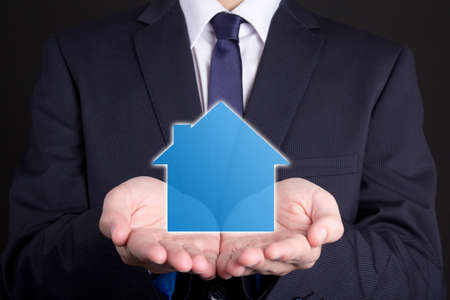 real estate concept - close up of business man holding small house in his handsの写真素材