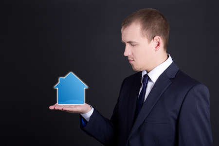 business man holding small house on his hand over grey backgroundの写真素材