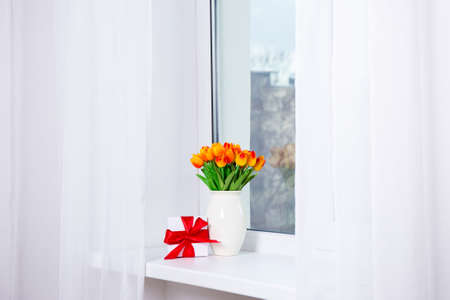 bunch of beautiful artificial tulips and gift box on a window sillの写真素材