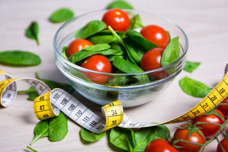 diet and weight loss concept - salad with spinach and tomatoes and measure tape on wooden table backgroundの写真素材