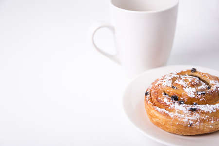 breakfast concept - sweet bun with raisins and cup of coffee or tea over white backgroundの写真素材
