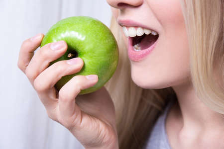 close up portrait of young woman biting green appleの写真素材
