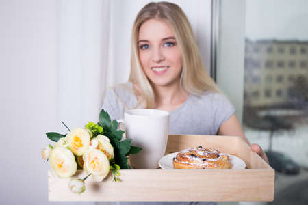 young woman bringing breakfast on wooden trayの写真素材