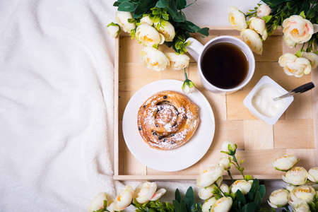 top view of breakfast with sweet bun, tea and yoghurt on wooden tray