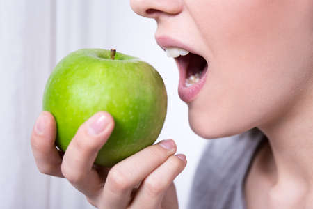 close up portrait of young beautiful woman biting green appleの写真素材