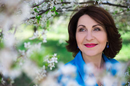 close up portrait of happy middle aged woman in blooming summer gardenの写真素材
