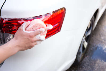 close up of male hand washing rear lights of white car by spongeの写真素材