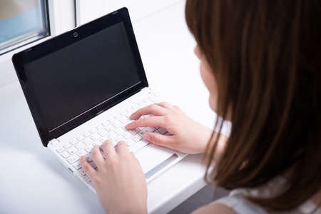 back view of young woman using laptop with blank screen