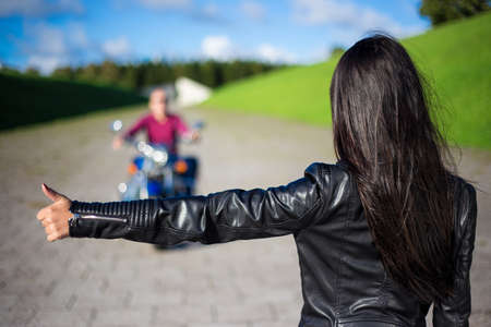 hitchhiking concept - back view of young woman hitching man on motorcycle on the roadの写真素材