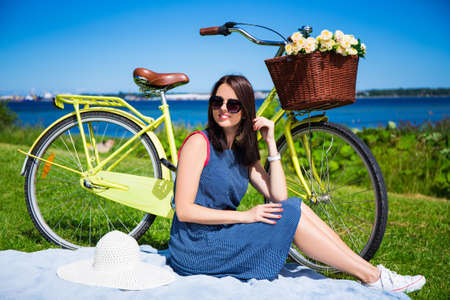 happy young woman sitting on the grass with vintage bicycle on the sea coastの写真素材