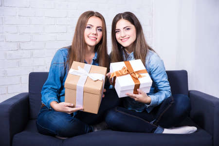 holidays and friendship - happy girls with gift boxes sitting on sofa at homeの写真素材