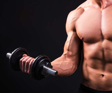 muscular man doing exercises with dumbbell over grey backgroundの写真素材