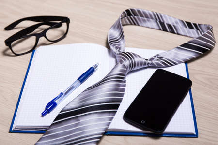 business concept - notebook, pen, glasses, tie and smart phone with blank screen