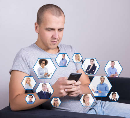 social media and internet addiction concept - handsome man sitting on sofa and using smart phoneの写真素材