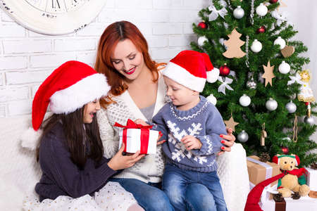 young mother giving presents to her kids in front of Christmas treeの写真素材