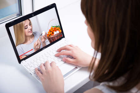 video blog concept - back view of woman watching on laptop video how to paint easter eggs at homeの写真素材