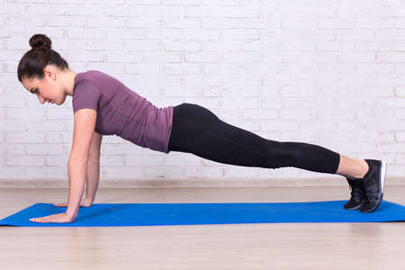 side view of young slim woman doing plank exercise at home