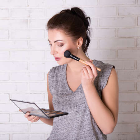 portrait of young beautiful woman applying make up over white wall