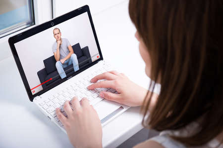 video blog concept - back view of young woman watching video on laptop at homeの写真素材