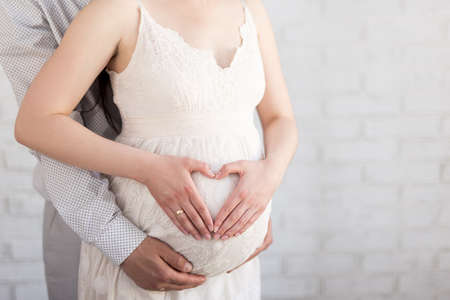 family, pregnancy and parenthood concept - couple making a heart shape with their hands on the pregnant bellyの写真素材