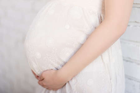 close up of pregnant woman touching her belly with hands over white