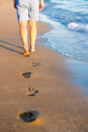 summer and vacation concept - walking man and footprints on the sunset beach in warm countryの写真素材