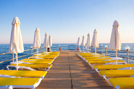 travel and vacation concept - wooden pier with chairs and umbrellas in blue seaの写真素材
