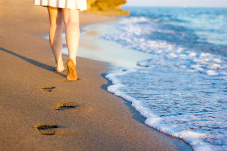 summer and travel concept - close up of female legs and footprints on the sunset beachの写真素材