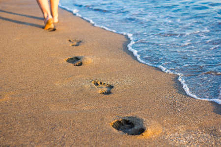 travel and vacation concept - legs, footprints in the sand and sea wave on the beachの写真素材