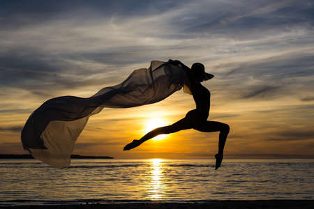 silhouette of slim sexy girl in bikini jumping with scarf on the beach at sunsetの写真素材